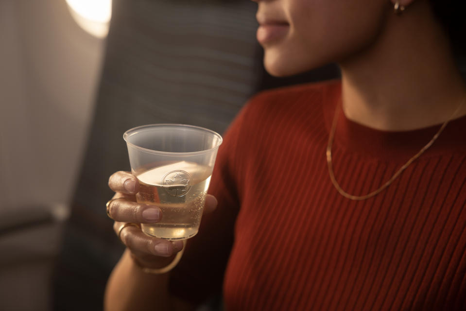 A woman is enjoying a drink and her Aeroplan member perks while on an Air Canada plane