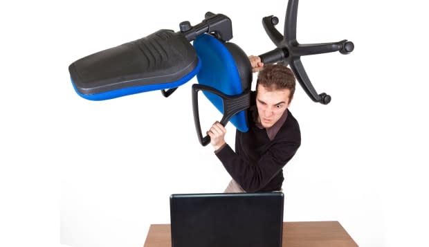 young angry man standing above a laptop with an office chair preparing to destroy it