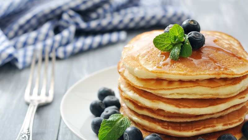 Pancakes with blueberries around them on a white plate with a fork next to it.