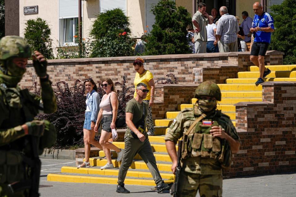 People walk past as Russian soldiers guard an office for Russian citizenship applications, in Melitopol, south Ukraine, July 14, 2022.