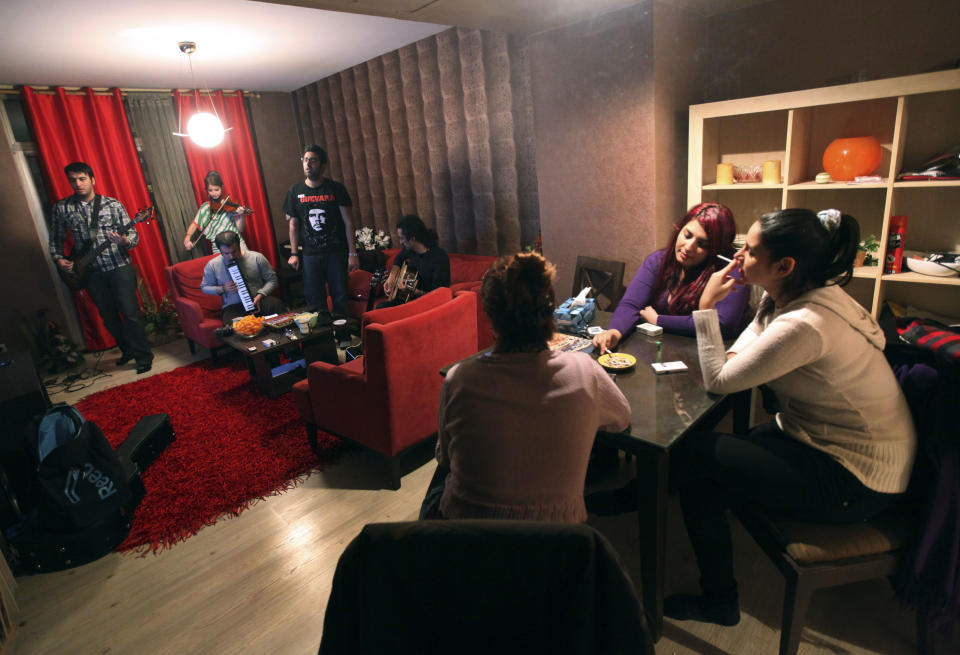 In this picture taken on Monday, Feb. 4, 2013, members of an Iranian band called "Accolade," group of five at left, practice as their friends listen to the performance at the house of one of their members in Tehran, Iran. Headphone-wearing disc jockeys mixing beats. It’s an underground music scene that is flourishing in Iran, despite government restrictions. (AP Photo/Vahid Salemi)