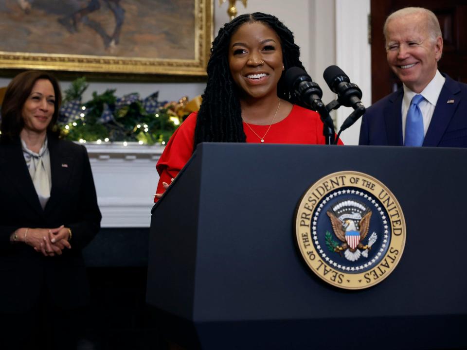 Cherelle Griner smiles standing at a dais at a press conference alongside President Joe Biden and Vice President Kamala Harris.