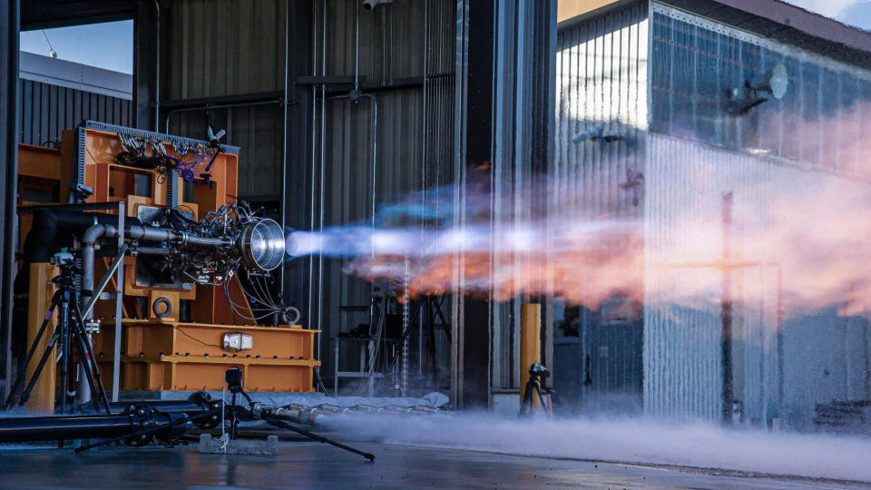 a horizontally placed rocket engine blasts out blue-orange exhaust during a static-fire test.