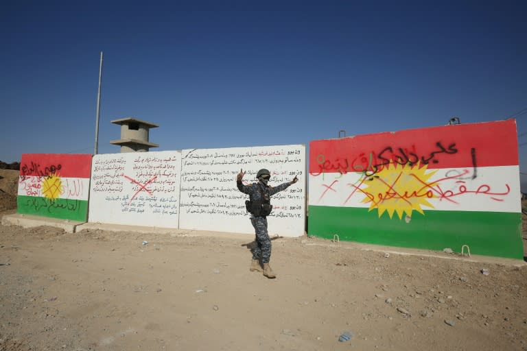 A member of the Iraqi forces walks past a defaced Kurdish flag on the outskirts of Kirkuk on October 16, 2017