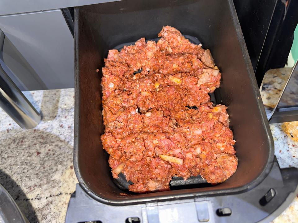 Raw ground meat in an air fryer basket.