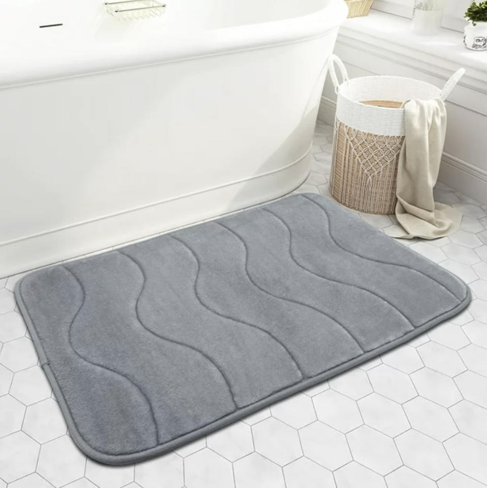 Memory foam bath mat on a tiled bathroom floor next to a tub and woven trash bin