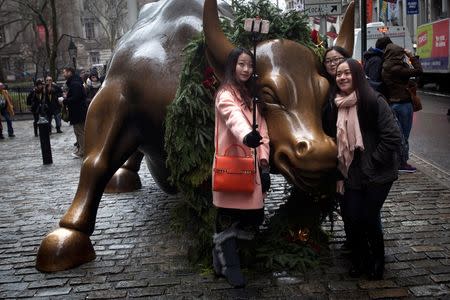 Tourists pose for photos with the Wall Street bull in Manhattan, New York, December 23, 2014. REUTERS/Carlo Allegri