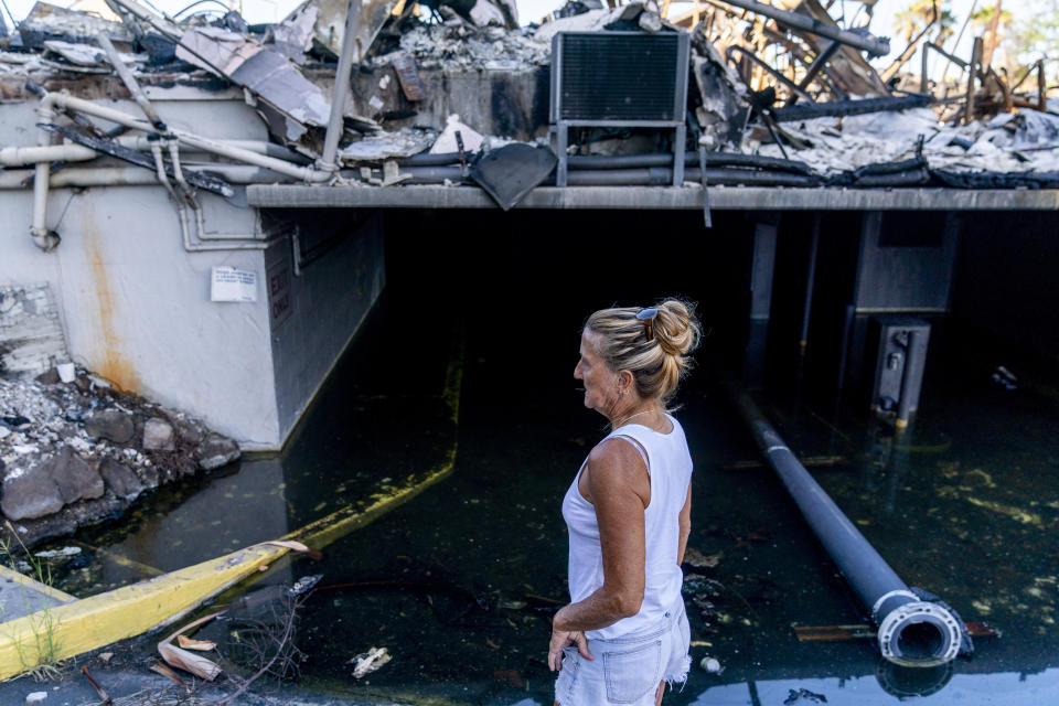 FILE - Janet Spreiter, whose home across the street was destroyed in the August wildfire, stands in front of a flooded parking garage in a destroyed business complex next to the Lahaina Shores Beach Resort on Front Street, Friday, Dec. 8, 2023, in Lahaina, Hawaii. Spreiter and other residents say they have concerns about the water with wildfire debris and toxins potentially seeping into the ocean or being pumped uphill to a tank that could seep into groundwater. (AP Photo/Lindsey Wasson, File)