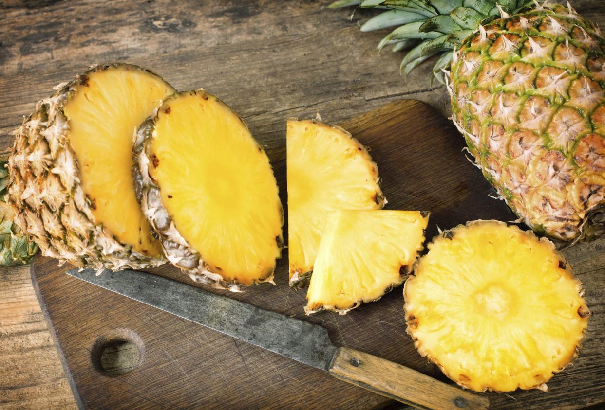 One whole and one sliced pineapples on wooden background.