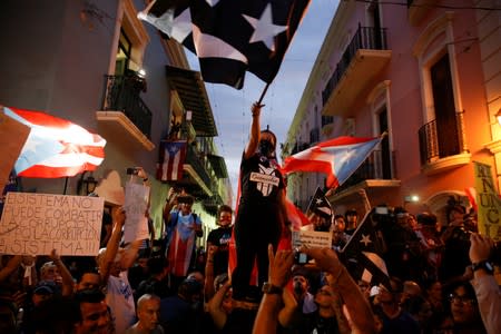 FILE PHOTO: A hooded demonstrator waves a Puerto Rican flag during the seventh day of protest calling for the resignation of Governor Ricardo Rossello in San Juan