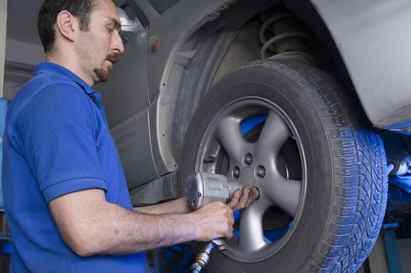 A mechanic changing a tire on a car that's up on a lift.