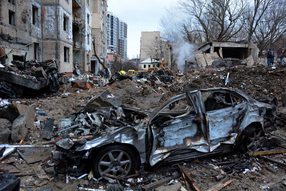 Destroyed vehicles in front of a damaged residential building
