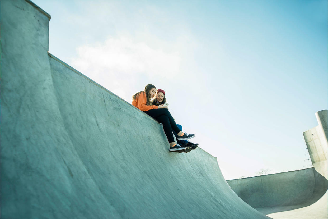 Two teenage girls in a skatepark, sharing a cell phone Getty Images/Westend61