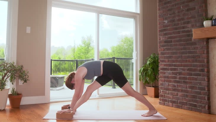 Yoga With Kassandra practicing a variation of Pyramid Pose with her hands on blocks during a 20-minute power yoga flow