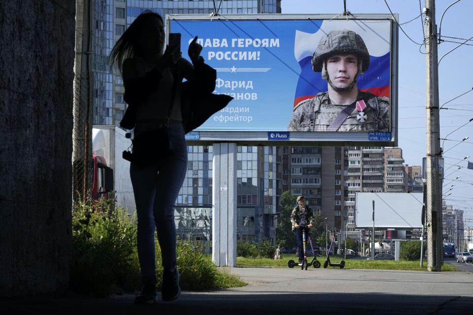 A woman uses her mobile phone as she walks past a billboard with a portrait of a Russian soldier and the words ‘Glory to the heroes of Russia’ in St. Petersburg, Russia, in August 2022. (AP Photo/Dmitri Lovetsky)