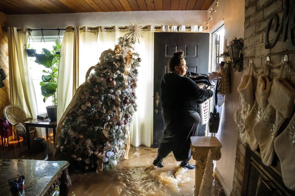 A woman carries belongings next to a tilted Christmas tree in a flooded living room