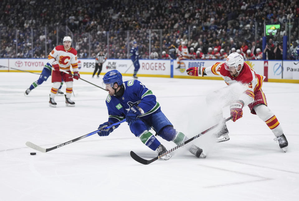 Vancouver Canucks' Conor Garland, left, turns away from Calgary Flames' MacKenzie Weegar while skating with the puck during the second period of an NHL hockey game Tuesday, April 16, 2024, in Vancouver, British Columbia. (Darryl Dyck/The Canadian Press via AP)