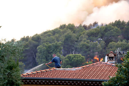 A man waters the roof of his house with a garden hose as flames and smoke from a burning wildfire are seen nearby in Carros, near Nice, France, July 24, 2017. REUTERS/Eric Gaillard