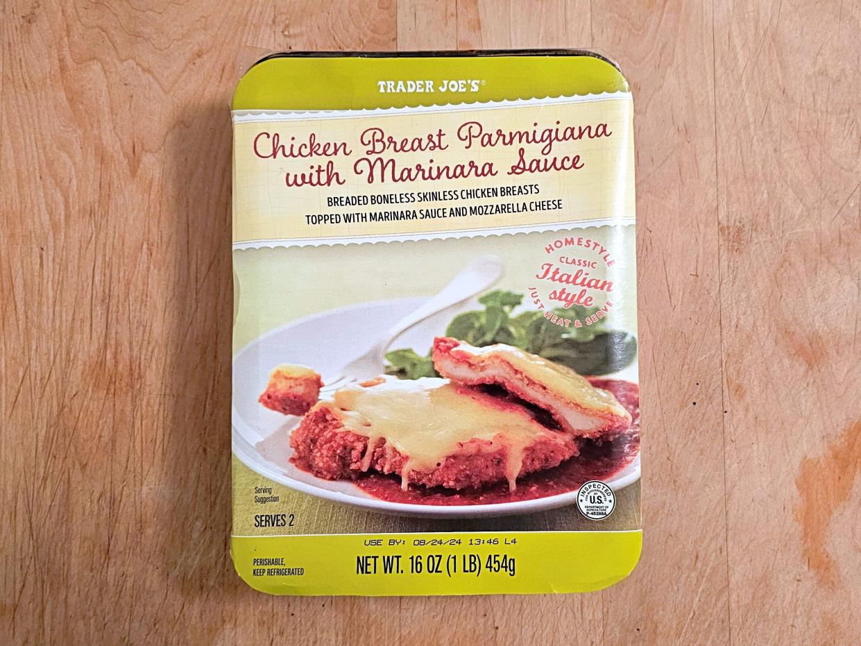 A box of  Trader Joe's chicken breast parmigiana with marinara sauce against a wooden background.