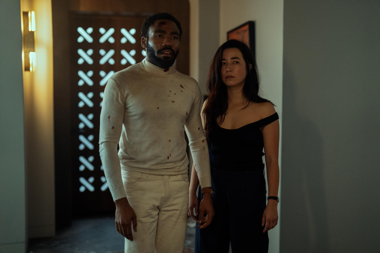 A battle-weary Donald Glover and Maya Erskine stand in a doorway. 