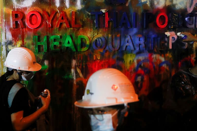 Demonstrators spray-paint a plaque with lettering on it in front of the police headquarters during a rally in Bangkok