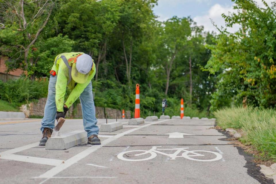 Crew members from Parrish and Sons Construction install parking blocks for the new bike lanes along Hickman Mills Drive on Friday, Aug. 5, 2022, in Kansas City.