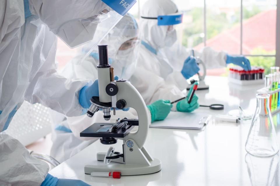 Scientists and microbiologists with PPE suit and face mask hold test tube and microscope in lab