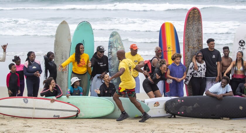 Huntington Beach, CA - Nathan Fluellen, center, founder of "A Great Day in the Stoke," an effort to highlight Black surfers and Black surfing history, high-fives surfers posing for an large group photos during the event at the Huntington Beach pier Friday, June 3, 2022. The event was billed as the "largest gathering of Black surfers in history" and was intended to inspire the Black community to feel welcome in the water and to experience and share the joy of surfing the waves safely as well as paying homage to veteran Black surfers who have been surfing since the 1950's. Surfers started the morning with a surf competition, free yoga lessons, and free surf lessons. The inaugural AGDITS aimed to create a safe space for Black surfers to connect, compete in a surf competition, recognize and award leaders in the community, provide free surf lessons, and capture an iconic photo of 500 black surfers similar to A Great Day in Harlem (1958) and A Great Day in Hip-Hop (1998) A Great Day in the Stoke welcomes all BIPOC (Black, Indigenous, and People of Color) communities and allies to surf in unity. (Allen J. Schaben / Los Angeles Times)