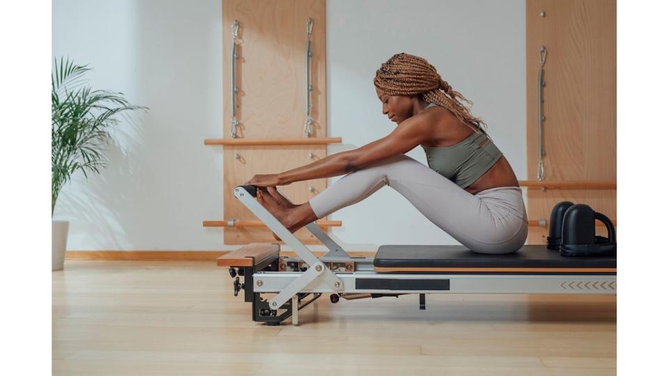  woman touching toes while doing pilates exercise on reformer.