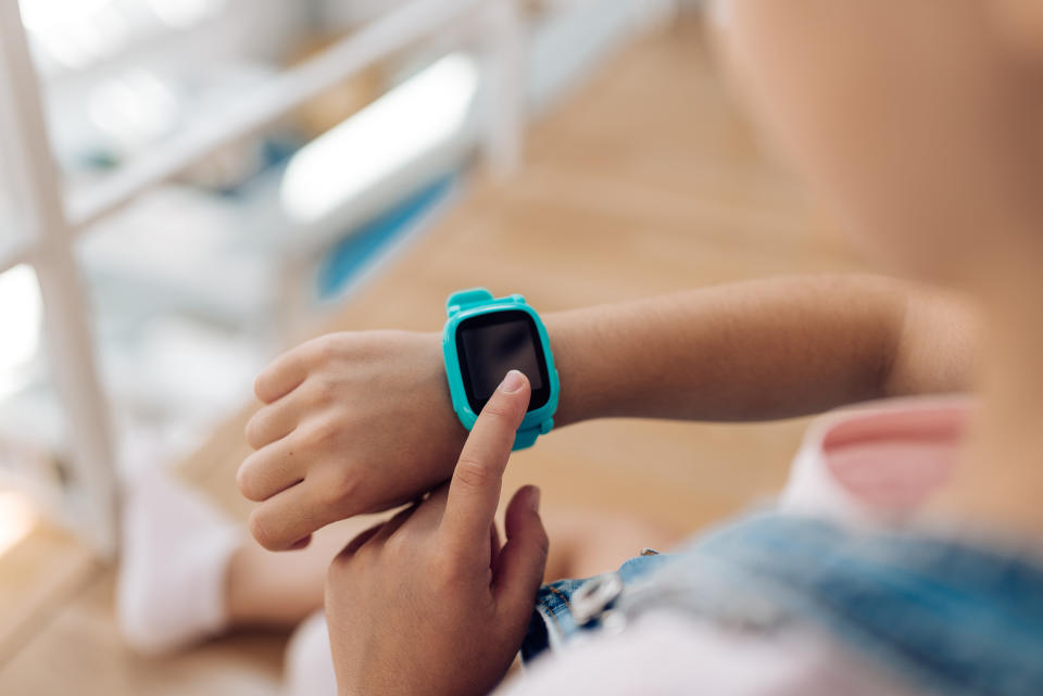 Unidentifizierbares Mädchen nutzt eine blaue Smartwatch am Handgelenk, Blick über linke Schulter