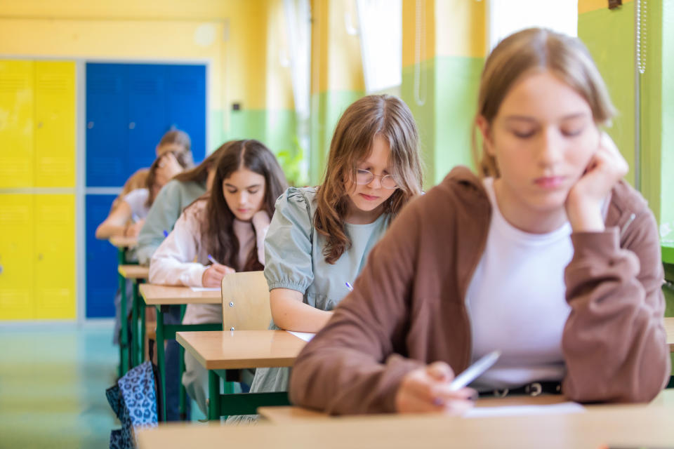 Teenage girls sitting in a row at the desks in the classroom and writing an exam.