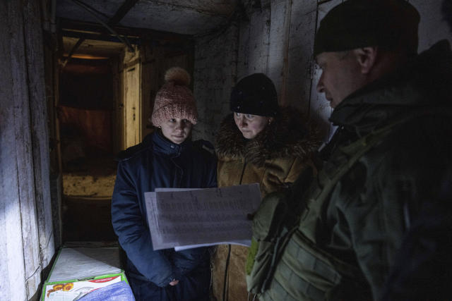 A Ukrainian police officer of the White Angels unit, tries to persuade Yulia Korotkova and her daughter Anya to evacuate to a safe area, as they stand inside a basement in Krasnohorivka, Ukraine, Tuesday, Feb. 21, 2023. Korotkova has lived with her daughter in the basement for more than a year. (AP Photo/Evgeniy Maloletka)