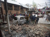 Kashmiri villagers gather near a car and a house that was damaged during a gun battle between government forces and suspected rebels in Bijbehara, some 28 miles (45 kilometers) south of Srinagar, Indian controlled Kashmir, Sunday, April 11, 2021. (AP Photo/Mukhtar Khan)