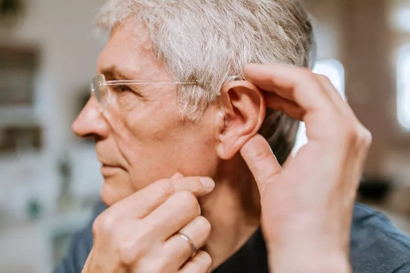 An older man is having a hearing aid fitted into his left ear.