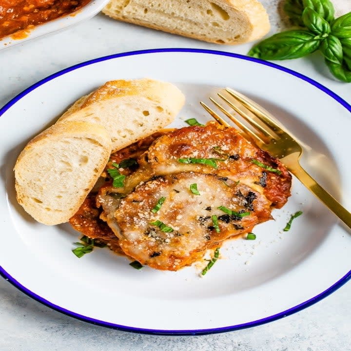 A plate with a slice of eggplant parmesan and bread on the side