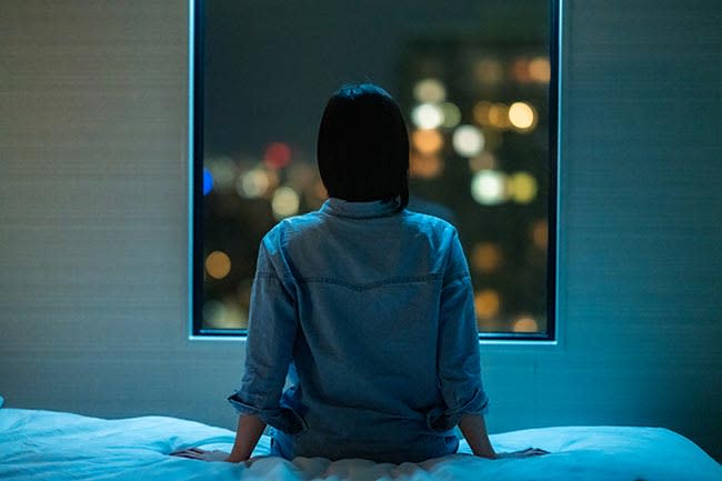 Mujer sentada por la noche al borde de la cama mirando por la ventana