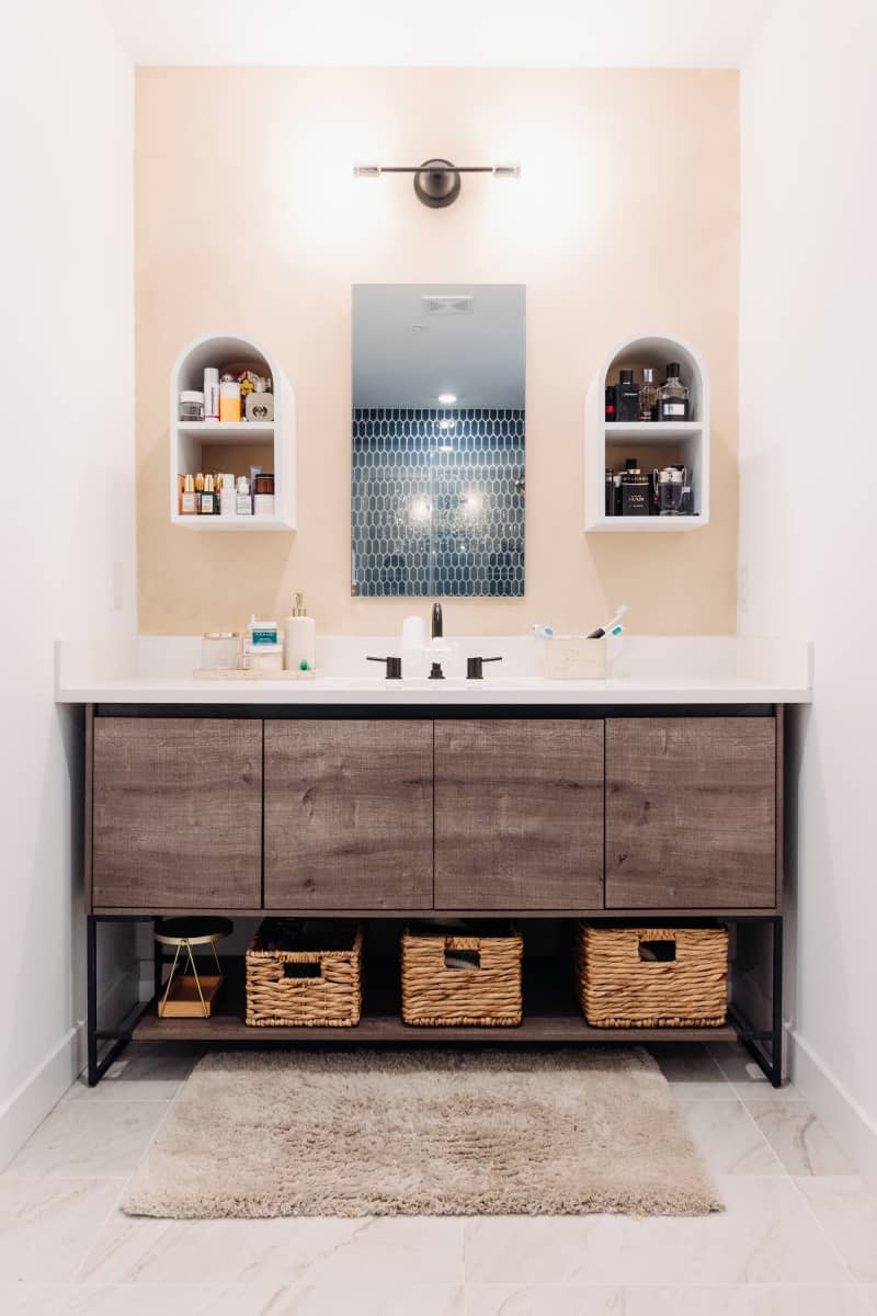 White bathroom with pale peach or beige accent wall behind sink with curved wall shelves