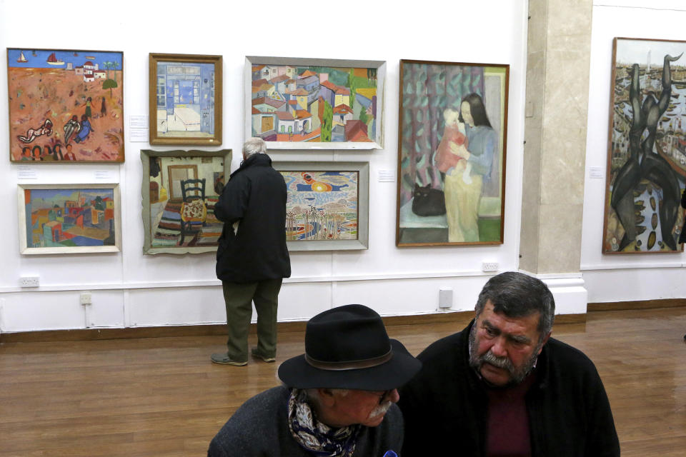 A man looks at paintings as during an exhibition of culturally significant paintings and audio visual recordings that were recently exchanged as part of an effort to boost confidence between the ethnically divided island nation's two communities, at the Ledra Palace Hotel inside the UN controlled buffer zone in divided capital Nicosia, Cyprus, Monday, Feb. 3, 2020. (AP Photo/Petros Karadjias)