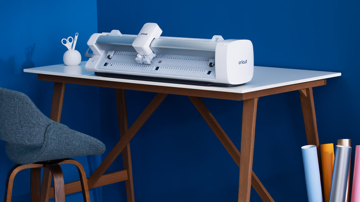  Cricut Venture: everything you need to know; a white craft machine on a desk against a blue wall. 