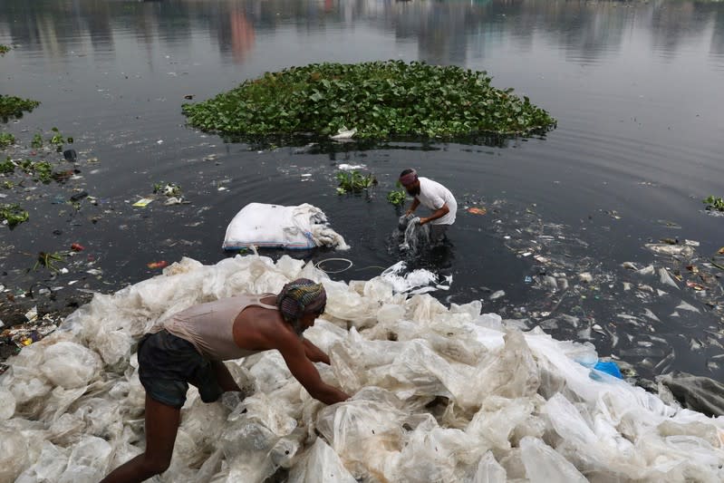 FILE PHOTO: Men wash plastic waste in the waters of the Buriganga river before recycling it, in Dhaka