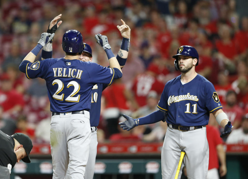 Milwaukee Brewers' Christian Yelich (22) is congratulated at the plate by Yasmani Grandal, obscured, left, and Mike Moustakas (11) following a two-run home run off Cincinnati Reds relief pitcher Robert Stephenson during the ninth inning of a baseball game, Monday, July 1, 2019, in Cincinnati. (AP Photo/Gary Landers)