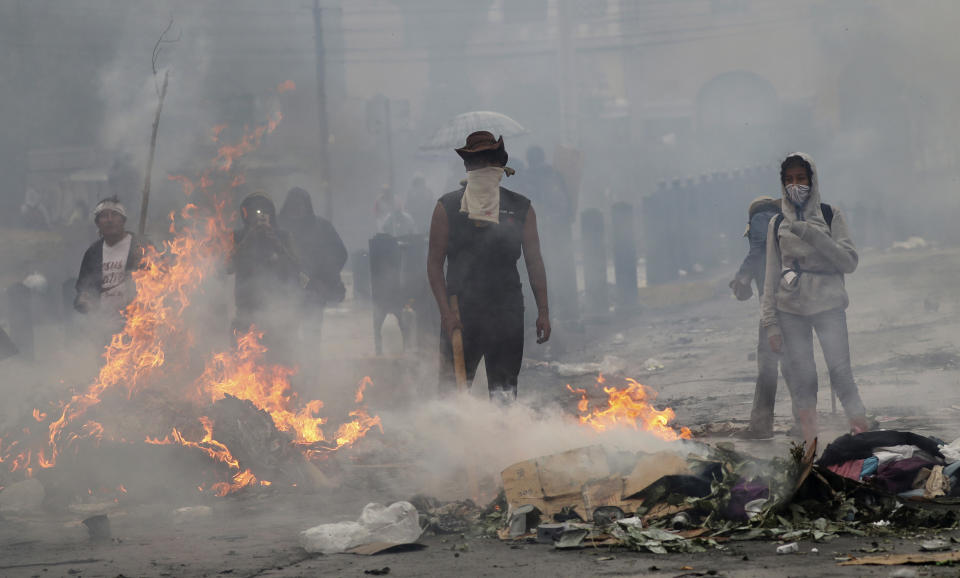 Anti-government protesters stand behind their burning roadblock as they face off with police near the National Assembly during a military curfew in Quito, Ecuador, Sunday, Oct. 13, 2019. Deadly protests against a plan to remove fuel subsidies as part of an International Monetary Fund austerity package have gone on for more than a week. (AP Photo/Dolores Ochoa)