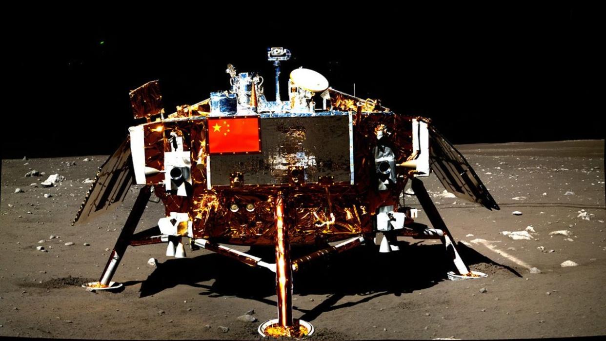  A cube-shaped spacecraft covered in gold foil sits on the surface of the moon atop four legs. 