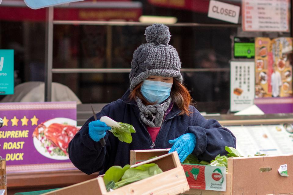 A worker wears a surgical face mask as she prepares vegetables on a stall in London's China Town district.