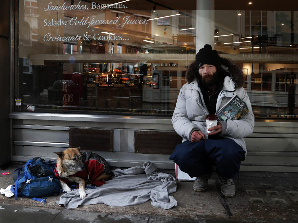 A homeless person and his dog rest outside a coffee shop in London, Monday, Feb. 8, 2021. In the battle against COVID-19, the homeless are not listed among the British government's highest priority groups for the vaccine rollout — currently people over 70 years old, care home residents, frontline health and social care workers, as well as the clinically vulnerable. (AP Photo/Frank Augstein)