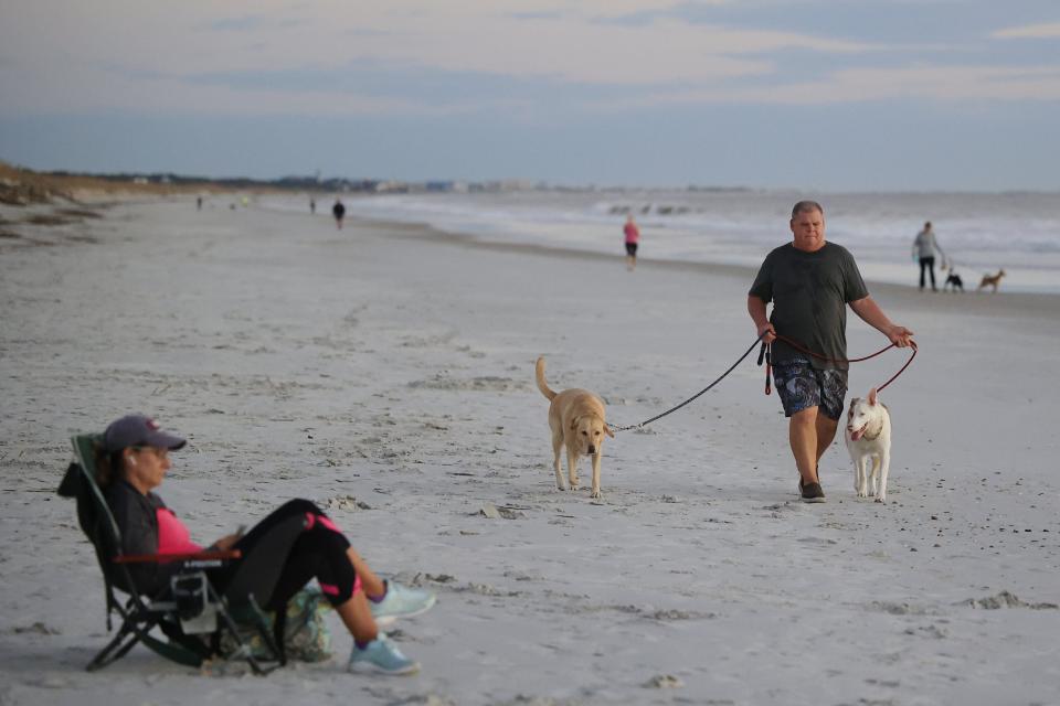 The beach at Atlantic Beach is busy even in the early morning, as seen on Wednesday as Kerry Russell walks his dogs Luna, on left, and  Tundra, passing a relaxing Kathy Laning. Atlantic Beach this week passed a ban on smoking at the beach and in parks.