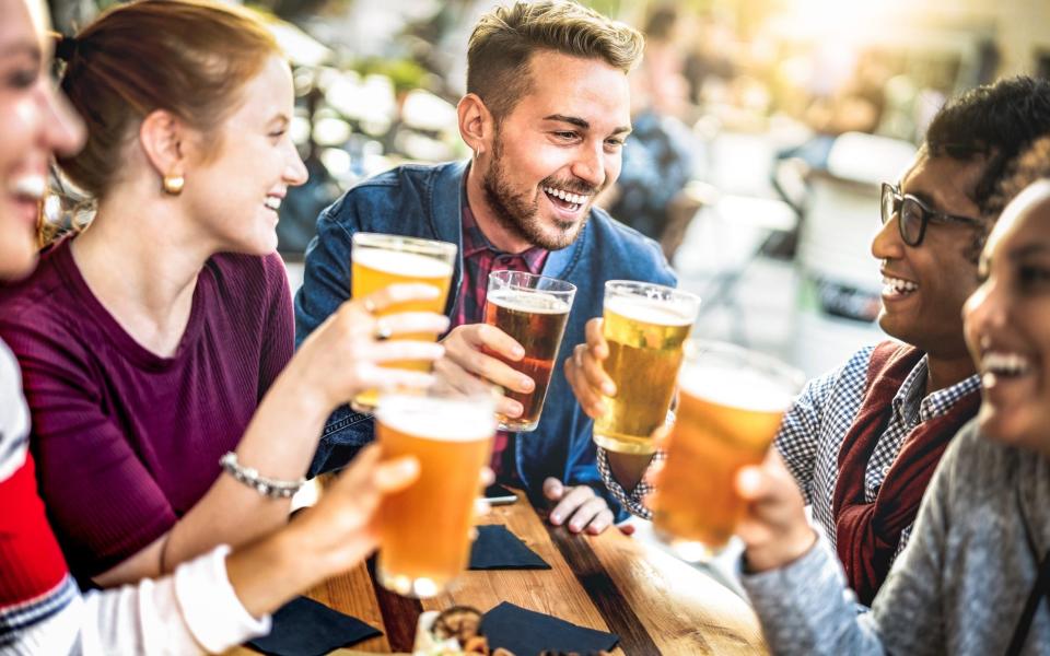 Young people drinking beer pints at brewery bar garden - Genuine beverage life style concept with guys and girls sharing happy hour together at open air pub dehor - Warm sunset backlight filter