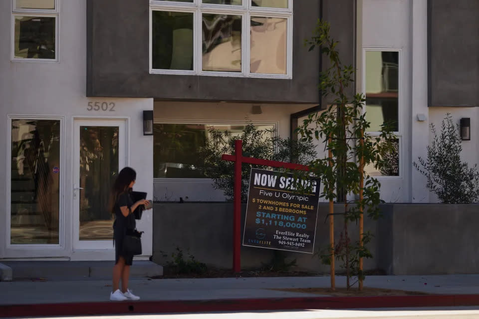 Una mujer de pie cerca de un cartel de ‘Se vende’ fuera de unos bloques de pisos en Los Ángeles, California (créditos: Allison Dinner, Getty Images).