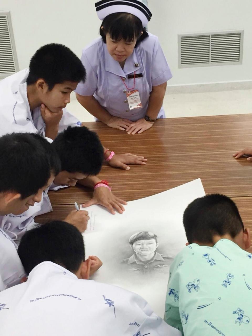 Some of the rescued football team autographs and write notes on a sketch of the Thai Navy SEAL diver who died while trying to rescue them (AP)