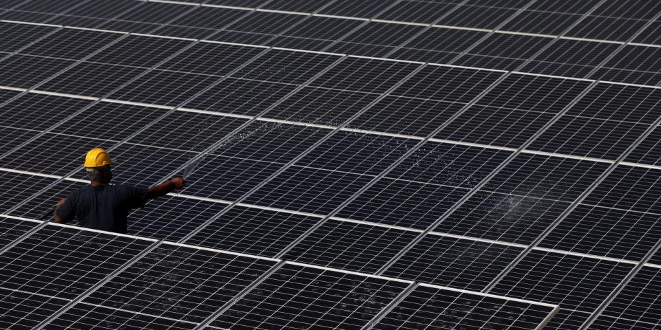 worker in yellow hard hat standing amid field of solar panels spraying water